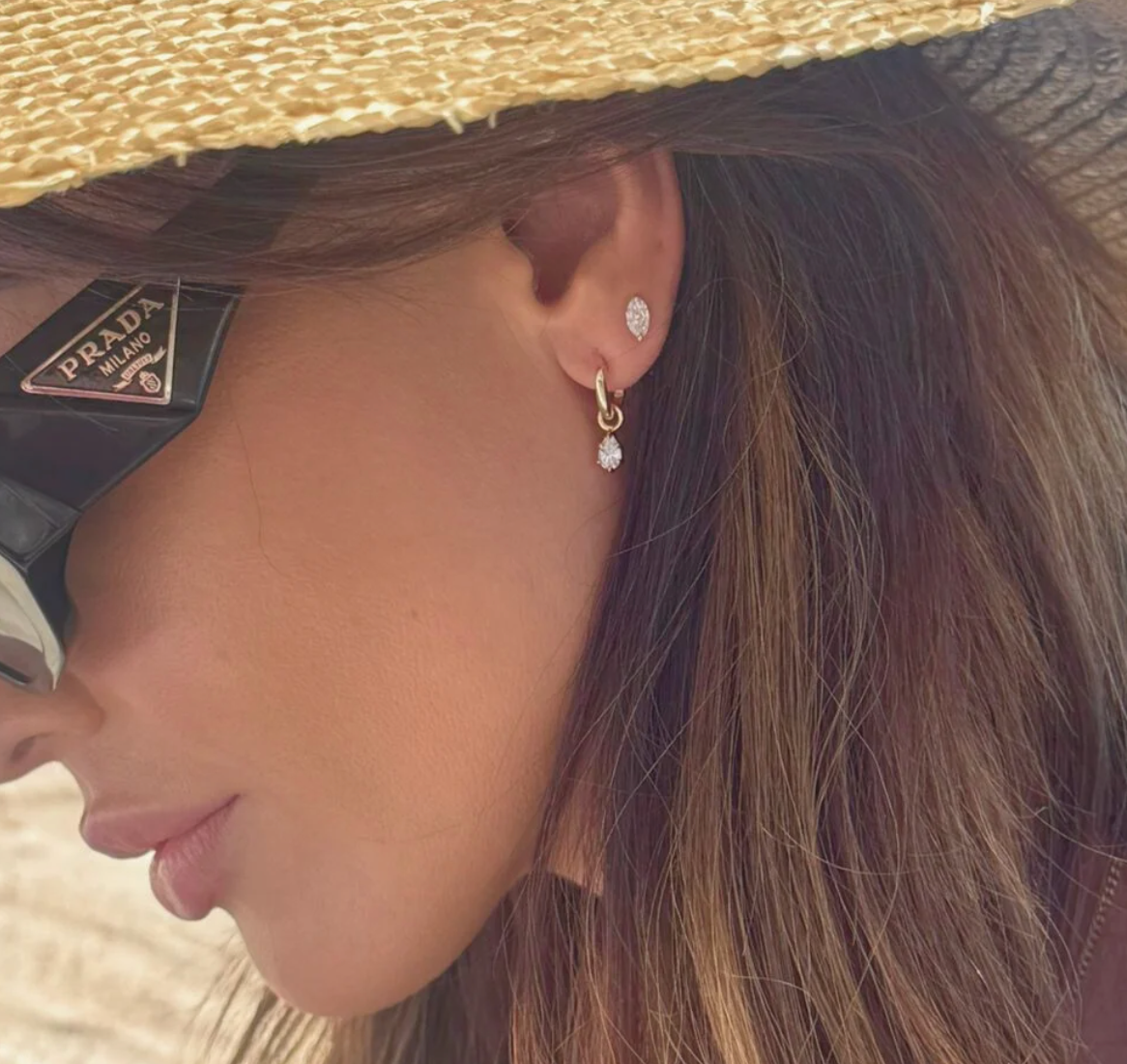 Close-up of a person wearing a Prada handbag, straw hat, and diamond earrings.