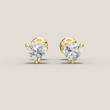 Heart-shaped diamond earrings with gold settings on a beige background