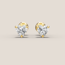 Heart-shaped diamond earrings with gold settings on a beige background