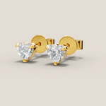 Gold heart-shaped diamond earrings on a beige background