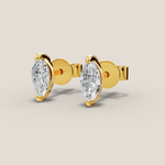 Gold earrings with pear-shaped clear gemstones on a beige background