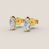 Gold earrings with pear-shaped clear gemstones on a beige background