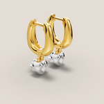Gold hoop earrings with silver heart charms on a beige background