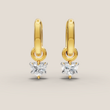 Gold hoop earrings with heart-shaped diamond drops on a beige background