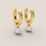 Gold hoop earrings with heart-shaped gemstones on a light beige background