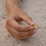 Hand holding a gold ring on a sandy surface