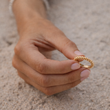 Hand holding a gold ring on a sandy surface