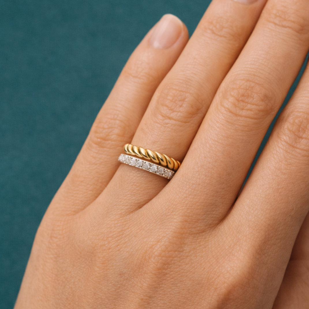 Hand wearing a gold and silver ring on a teal background