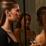 Woman holding a cocktail in front of a mirror with another woman's reflection.