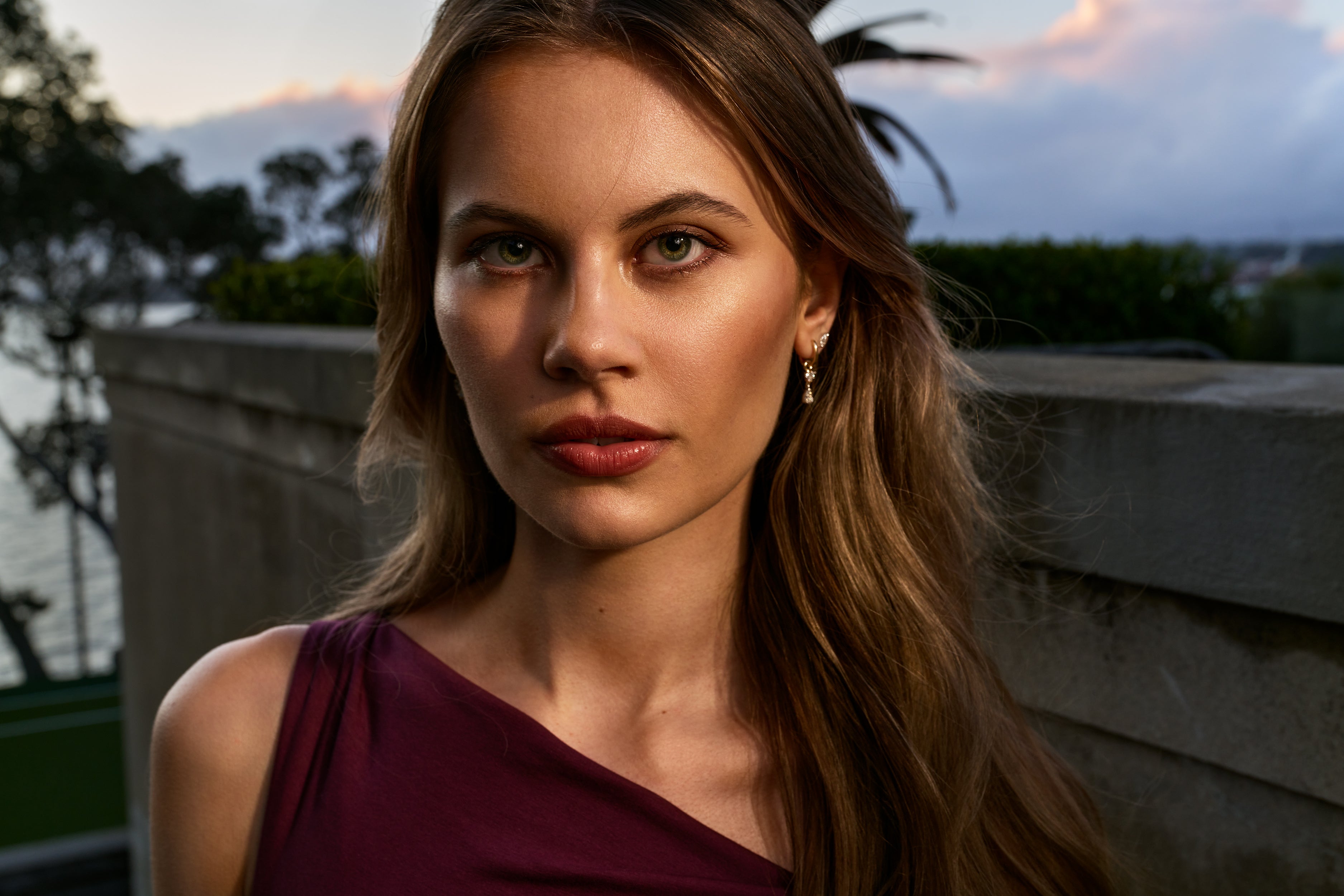 Woman with long brown hair wearing a burgundy dress outdoors during sunset.