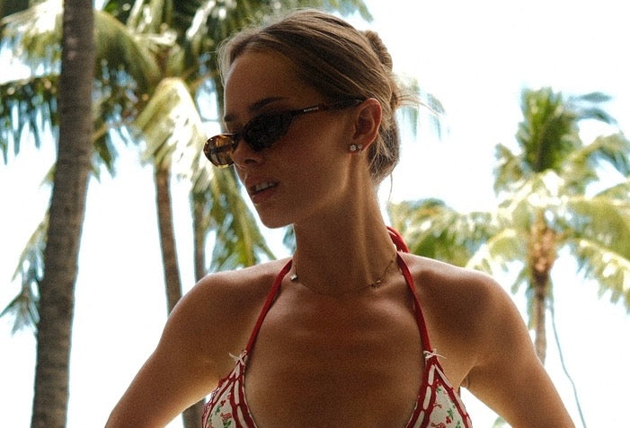 Woman wearing sunglasses and a red bikini top with palm trees in the background