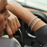 A woman's arm showing a tennis bracelet with multiple diamond charms, in a car interior.