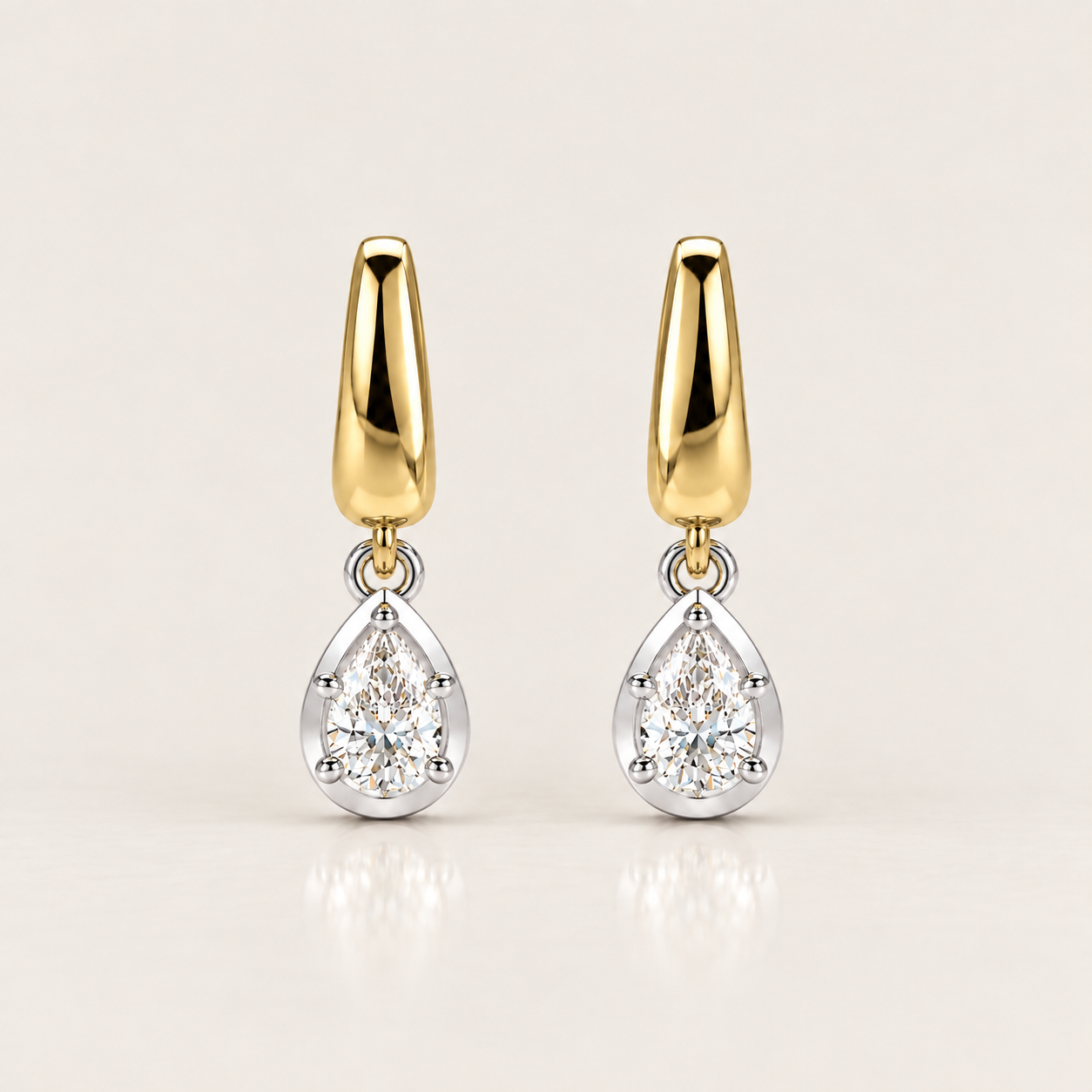 A pair of gold and silver drop earrings with pear-cut clear gemstones, displayed on a clean, light beige background.
