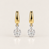 A pair of gold and silver drop earrings with pear-cut clear gemstones, displayed on a clean, light beige background.