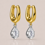 A pair of gold huggie hoop earrings with silver-toned settings holding clear teardrop-shaped gemstones, shown on a soft beige background.