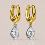 A pair of gold huggie hoop earrings with silver-toned settings holding clear teardrop-shaped gemstones, shown on a soft beige background.
